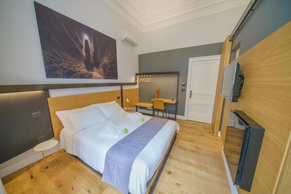 Ett modernt hotellrum med en stor säng, ett skrivbord, en stol och en tv.