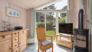 A cozy room with a wooden interior, a wicker chair, a TV, and a wood-burning stove. - Ferienhaus mit Sauna im Ferienpark Mirow (Mirow)