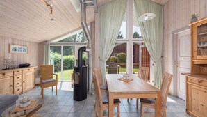 A cozy room with a wooden table and chairs, a sofa, a glass coffee table, and a fireplace. - Ferienhaus mit Sauna im Ferienpark Mirow (Mirow)