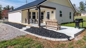 Un bâtiment d’un seul étage doté d’un porche couvert, d’un barbecue et d’un petit espace de détente avec un banc et des chaises.