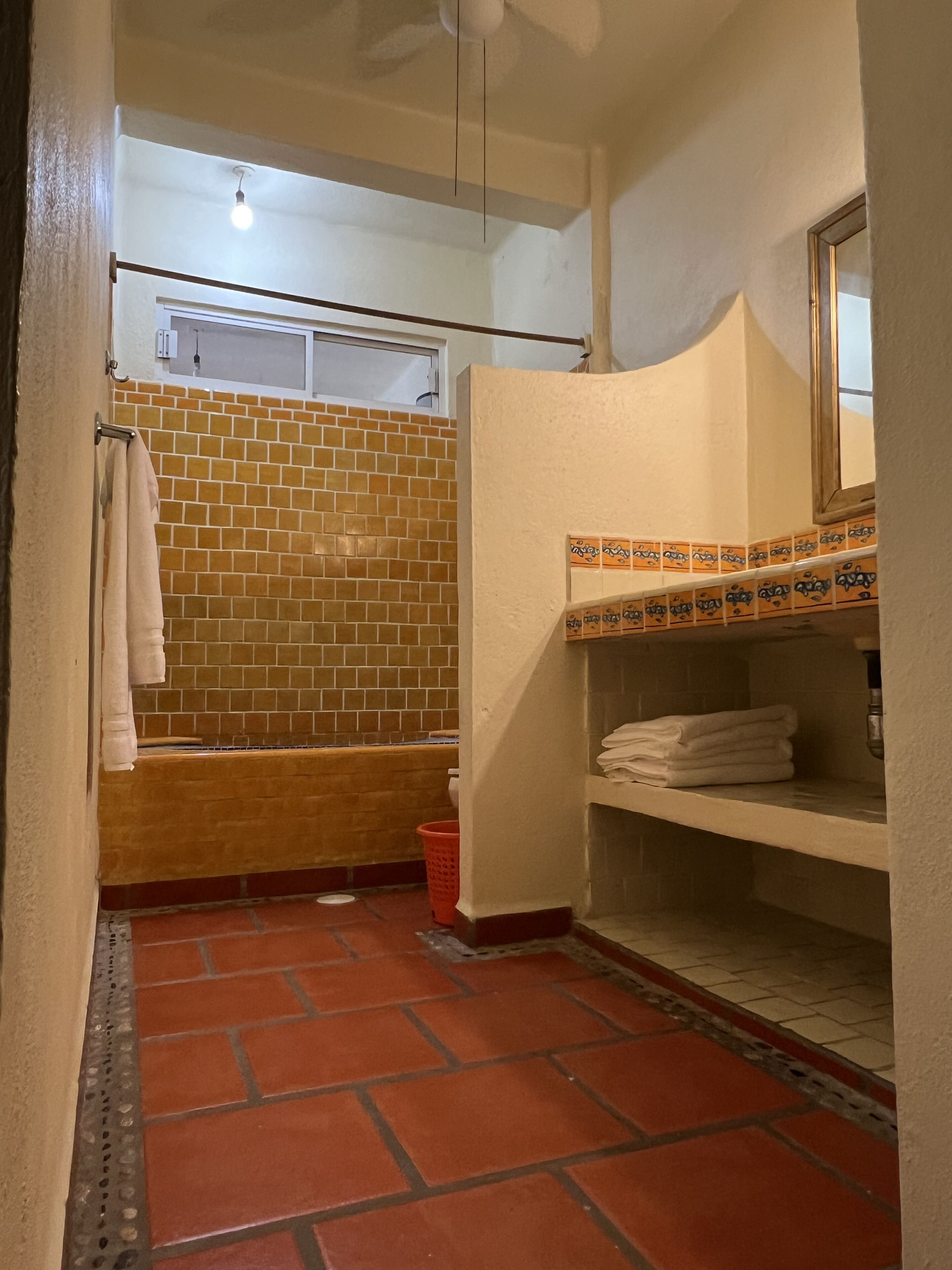 A bathroom with a tiled shower, a sink with a mirror, and a shelf with folded towels.