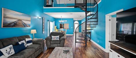A living room with a blue wall, a wooden coffee table, a sofa, a chair, a TV stand, and a spiral staircase.