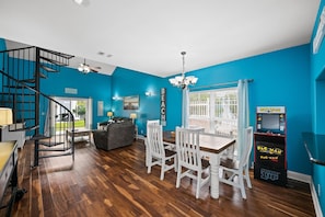 A room with a spiral staircase, a dining table with chairs, a couch, and a Pac-Man arcade machine. - Coral Retreat (Pensacola)