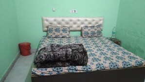 A bedroom with a bed, a red bucket, and a water bottle on a nightstand. - Hotel Hansi (Hansi)