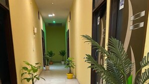 A hallway with potted plants, a tiled floor, and doors with numbers. - Hotel Hansi (Hansi)