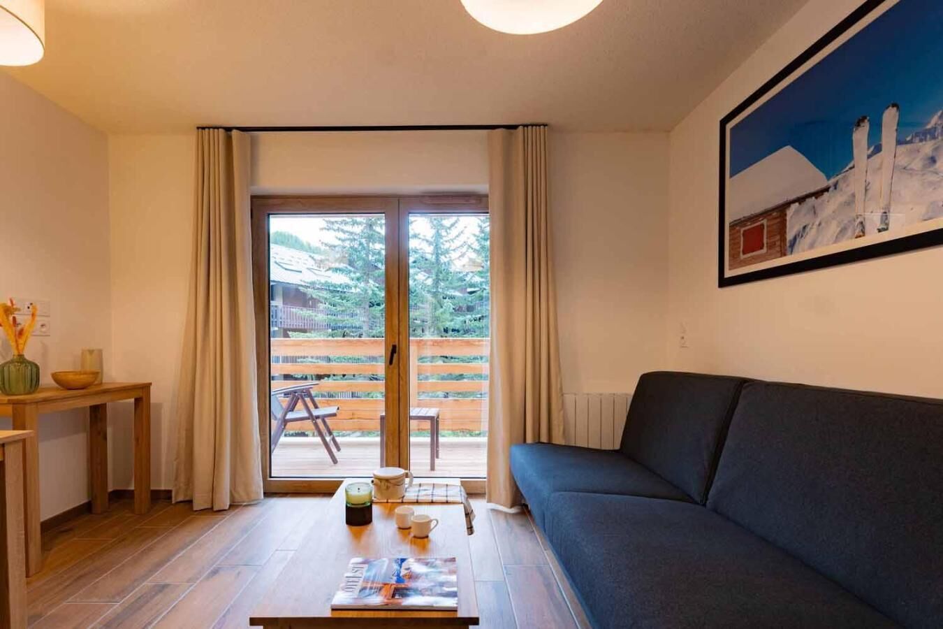 A living room with a dark sofa, a wooden table with a magazine, and a view of a wooden deck through a glass door.