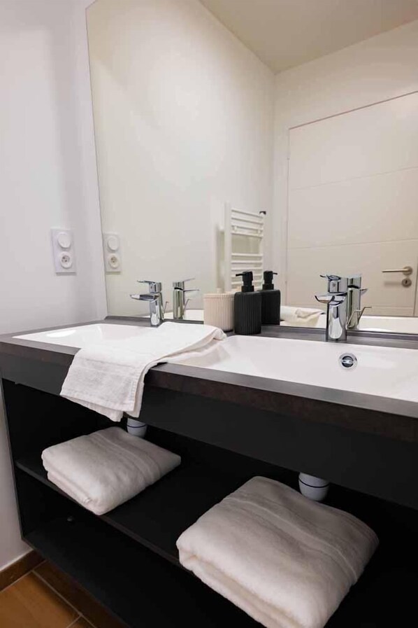 A modern bathroom with two sinks, a large mirror, and a towel rack.