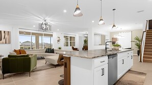 Une cuisine moderne dotée d’un îlot central, de luminaires suspendus et offrant une vue sur l’extérieur grâce à de grandes fenêtres.