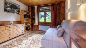 Une pièce chaleureuse avec un plafond en bois, un canapé, une bibliothèque et une fenêtre donnant sur une maison.