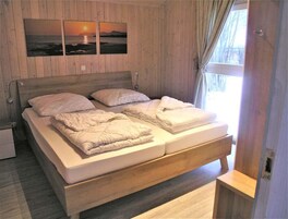 Un dormitorio con paneles de madera, una cama, almohadas y una mesita de noche.