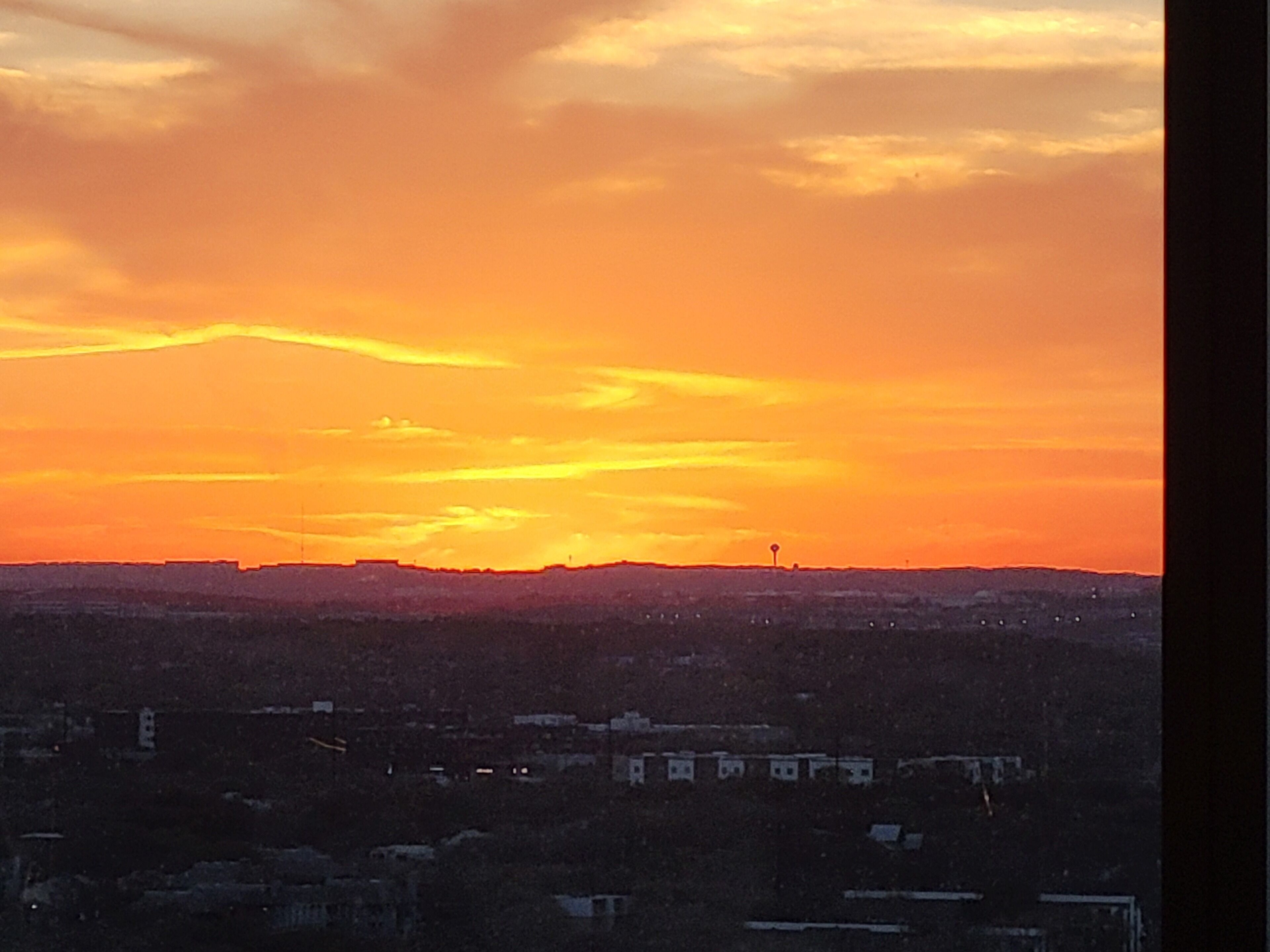 A sunset over a cityscape with buildings silhouetted against the sky.