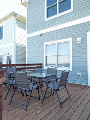 Un patio cubierto con una mesa y sillas, una terraza de madera y una casa con revestimiento azul y detalles blancos.