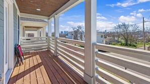 Una terraza de madera con barandillas blancas, una silla roja y una vista panorámica de la ciudad de fondo.