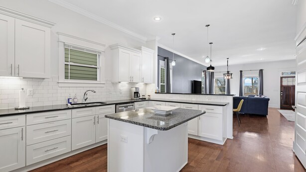 Una cocina moderna con armarios blancos, una isla central y un área de comedor con un sofá azul.