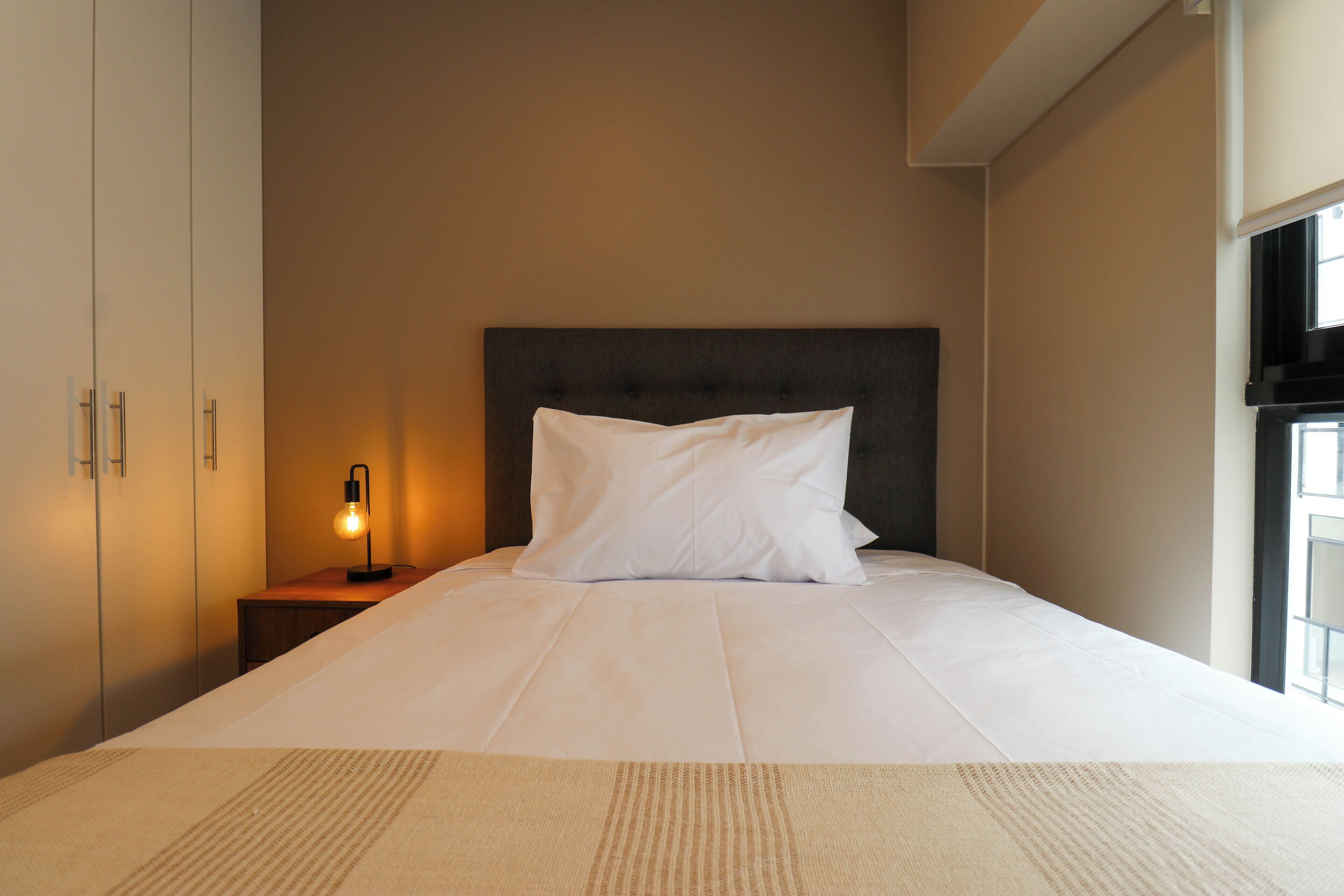 Una cama bien hecha con un almohadón blanco y un cabecero oscuro en una habitación de hotel.