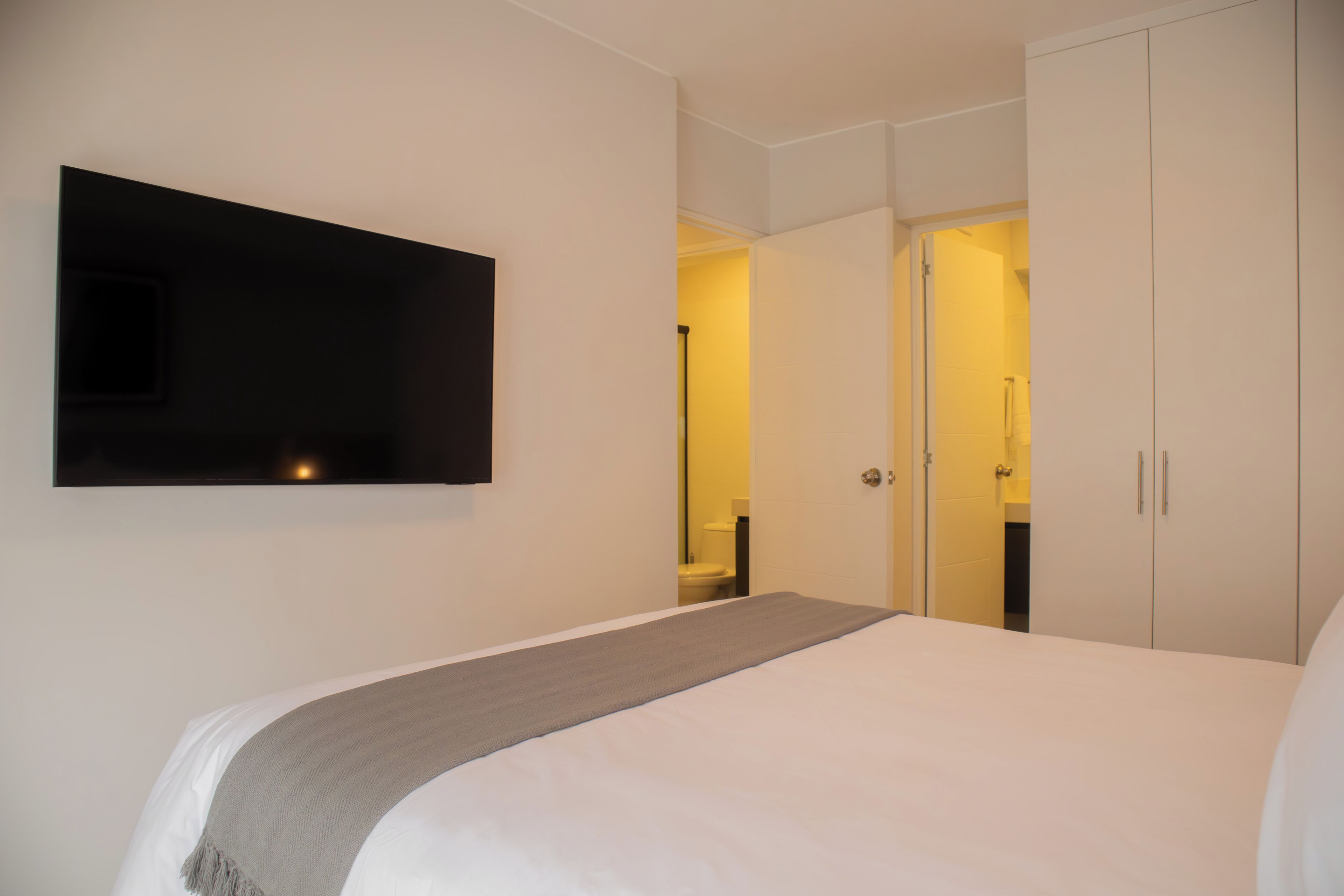 A hotel room with a bed, a TV mounted on the wall, and a wardrobe.