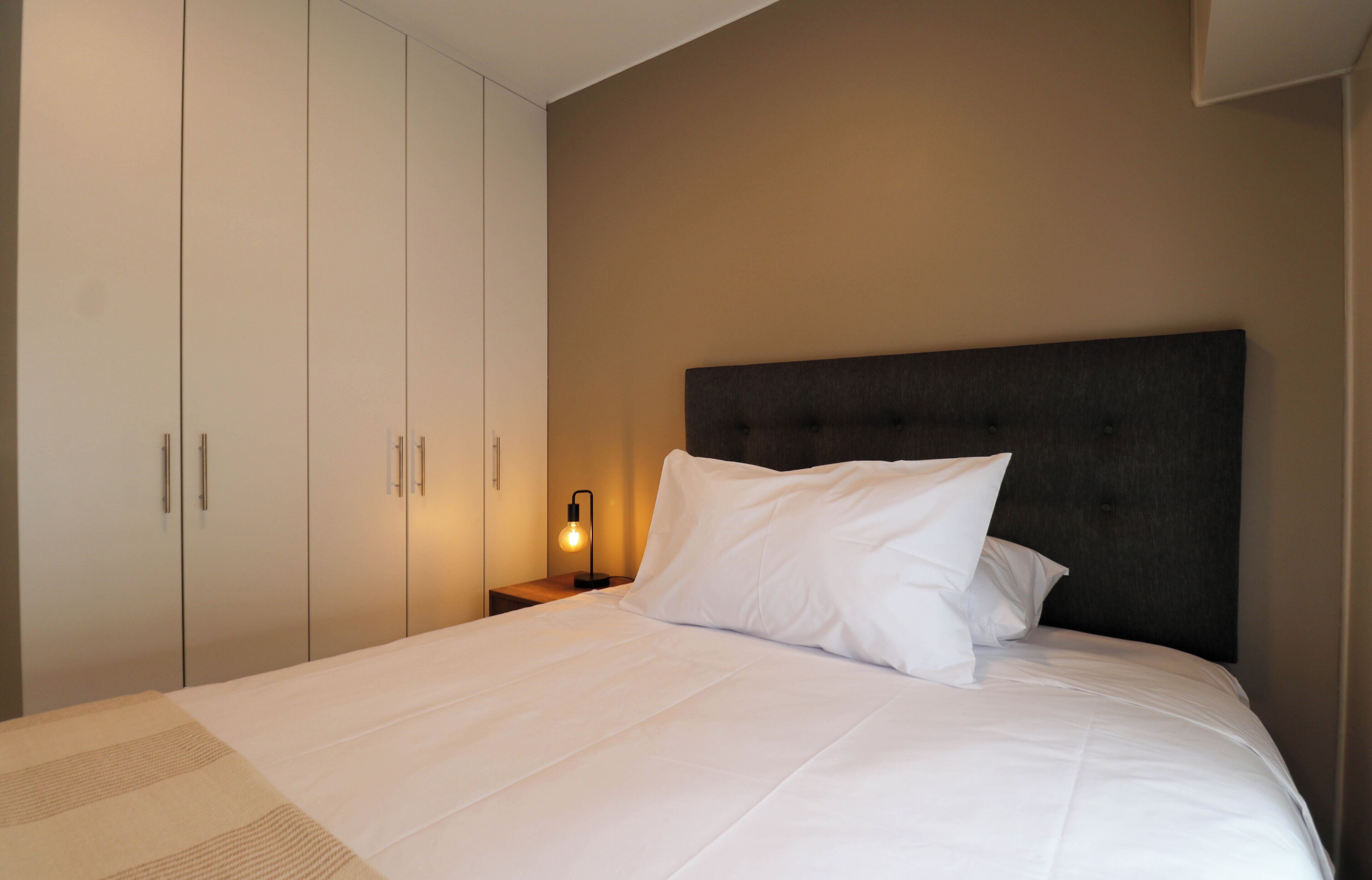 A bedroom with a bed, a nightstand with a lamp, and a wardrobe.