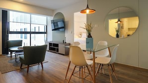 Una sala de estar moderna con una mesa de comedor de vidrio, dos sillas, un sofá y un televisor montado en la pared.