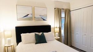A neatly made bed with white linens and a green pillow, two bedside lamps, and a window with curtains. - Goldenrod - Studio in Downtown Lexington (Lexington)