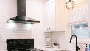 A kitchen with white cabinets, a black stove, and a window with blinds. - Goldenrod - Studio in Downtown Lexington (Lexington)