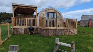 A rustic cabin with a wooden deck, a stone fire pit, and a covered seating area. - Galloway Steading Luxury Glamping Pods (Newton Stewart)