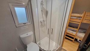 A bathroom with a toilet, a shower enclosure, a window, and a bunk bed. - Galloway Steading Luxury Glamping Pods (Newton Stewart)