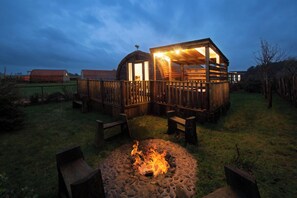A rustic wooden cabin with a fire pit in the foreground, surrounded by a wooden deck and benches. - Galloway Steading Luxury Glamping Pods (Newton Stewart)