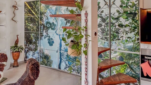Een modern interieur met een spiltrap, een groot raam met uitzicht op bomen, en een klein tafeltje met een bloempot.
