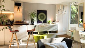 Een moderne woonkamer met een bank, stoelen, een eethoek en een keuken, inclusief een televisie en planten.