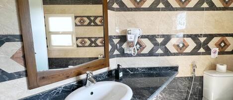 A bathroom with a white sink, black marble countertop, and patterned tile walls.