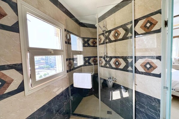 A modern bathroom with a glass shower enclosure, a sink, and a window providing natural light.