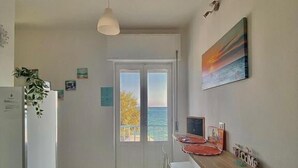 A kitchen with a stone floor, a white refrigerator, a dining table with chairs, a hanging light fixture, and a view through a glass door. - Acquamarina B&B Deluxe (Cariati)