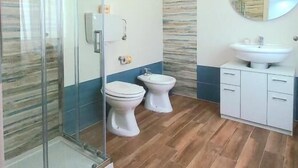 A bathroom with a glass shower enclosure, two toilets, a sink, and a mirror. - Acquamarina B&B Deluxe (Cariati)