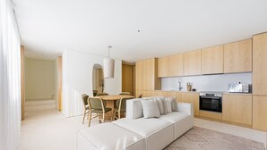 A modern kitchen with wooden cabinets, a dining area with a table and chairs, and a living area with a sofa and cushions. - GuestReady - DPV GuestHouse - Apart 6 (Porto)