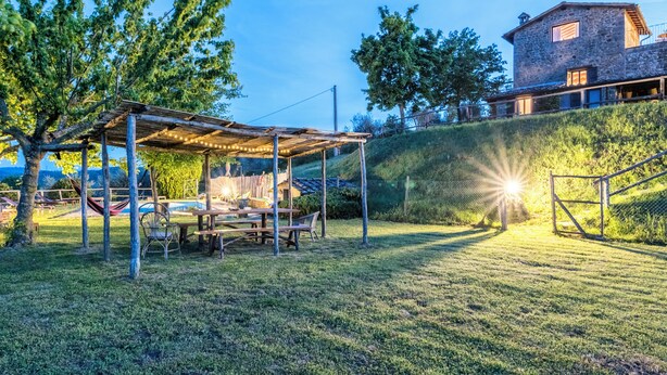 A covered outdoor seating area with tables and chairs, a hammock, and a stone building in the background.