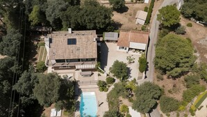Vista aérea de uma propriedade residencial com uma casa grande, piscina e vegetação ao redor.