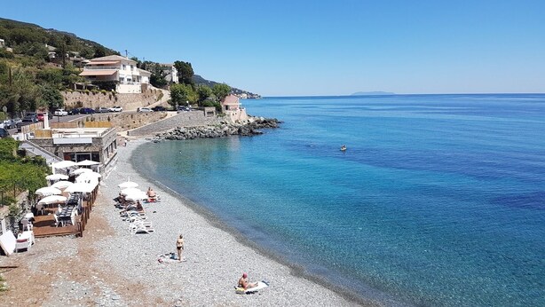 A pebble beach with umbrellas, a rocky shoreline, and buildings in the background. - Sublime ROOFTOP sea and mountain view on the heights of Bastia (Ville-di-Pietrabugno)