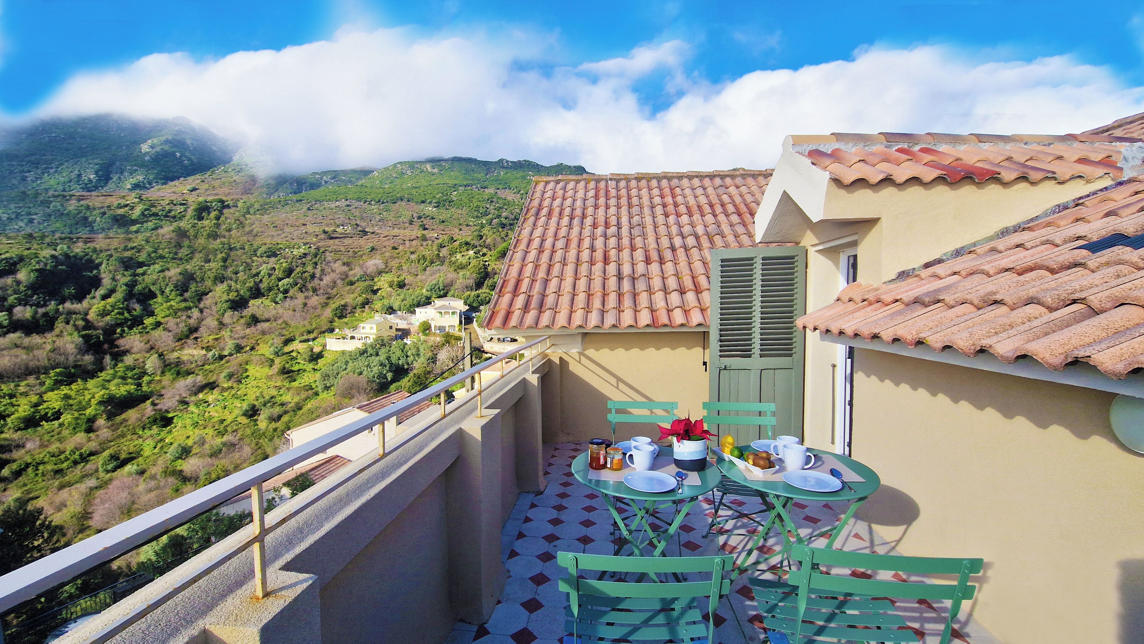Un balcon avec une table dressée pour deux personnes, offrant une vue sur un paysage montagneux et un village situé en contrebas.