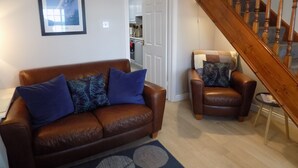 A living room with a brown leather sofa, a brown armchair, and a wooden staircase.