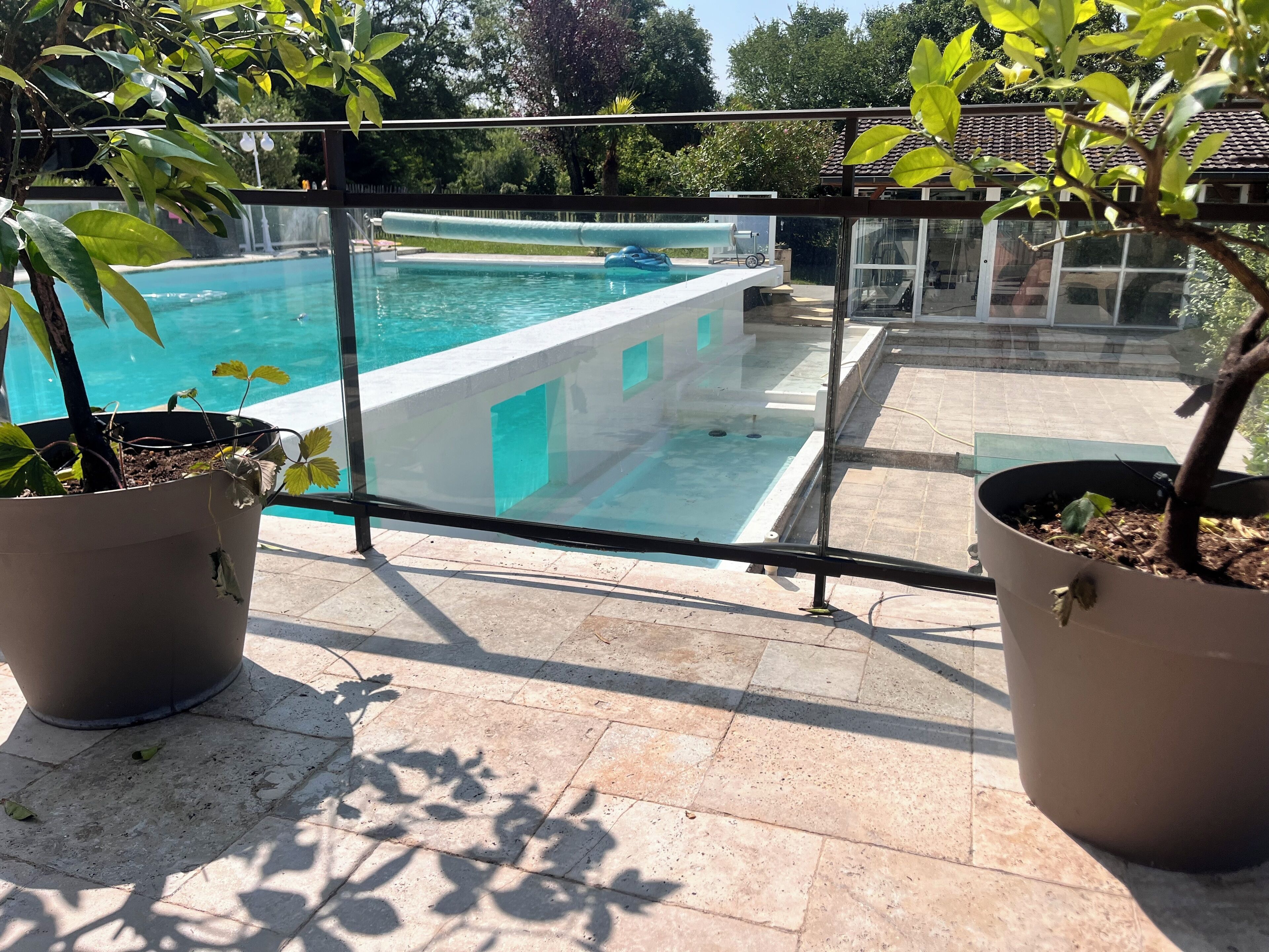 Un espace piscine agrémenté d’une barrière en verre, de plantes en pot et d’une terrasse carrelée.
