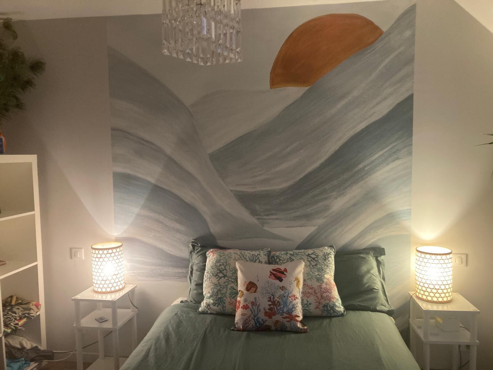 A bedroom with a bed, two nightstands, a chandelier, and a wall mural.