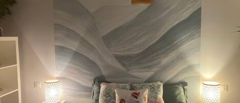 A bedroom with a bed, two nightstands, a chandelier, and a wall mural.