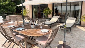 Un patio al aire libre con una mesa de madera preparada para comer, rodeado de sillones de descanso y una sombrilla grande que da sombra.