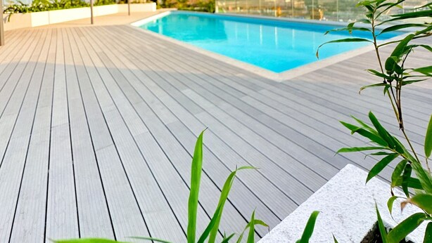 Uma área de piscina no terraço, com um deque de madeira, espaço de estar coberto e vista para o horizonte da cidade.
