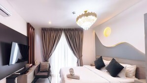 Quarto de hotel moderno com televisão de tela plana, escrivaninha, cadeira, cama com travesseiros, lustre e luminária na parede.