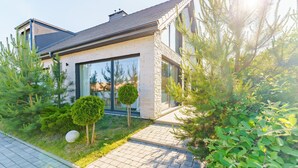 A modern house with a brick facade, large windows, and a well-maintained garden with various shrubs and a small tree.