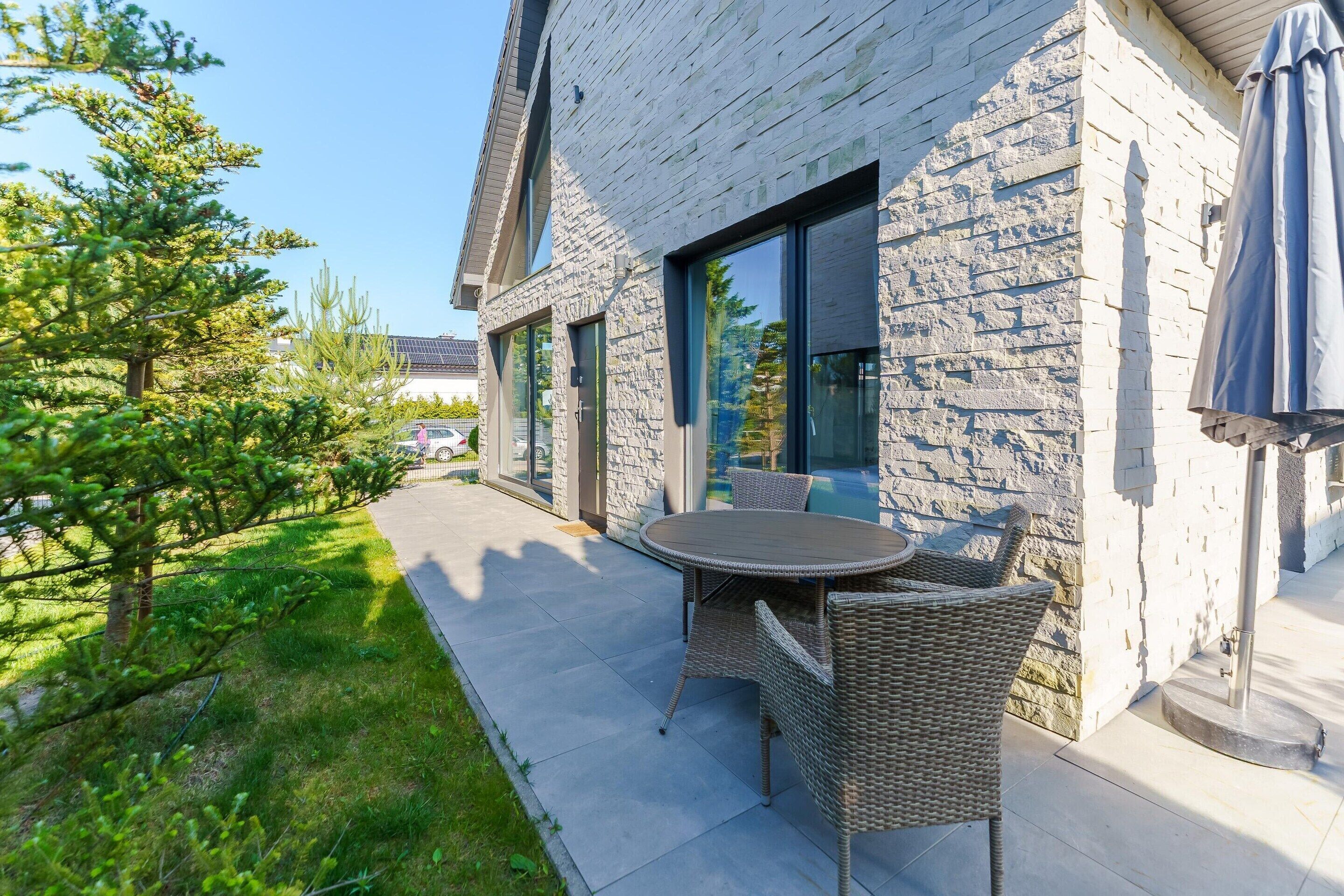 A modern house with a stone exterior, a patio with a table and chairs, and a large window.