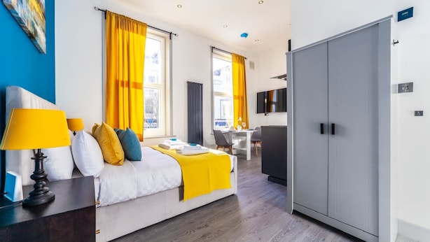 A hotel room with a bed, a desk, a wardrobe, and a TV. - Studio 2 - Gorgeous Studio in Earls Court (London)