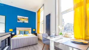 A modern hotel room with a bed, a dining table, and a view of the city. - Studio 2 - Gorgeous Studio in Earls Court (London)