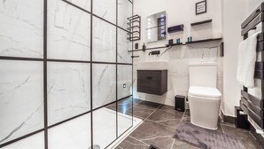 A modern bathroom with a glass shower enclosure, a white toilet, and a vanity with a mirror and shelves. - Studio 2 - Gorgeous Studio in Earls Court (London)